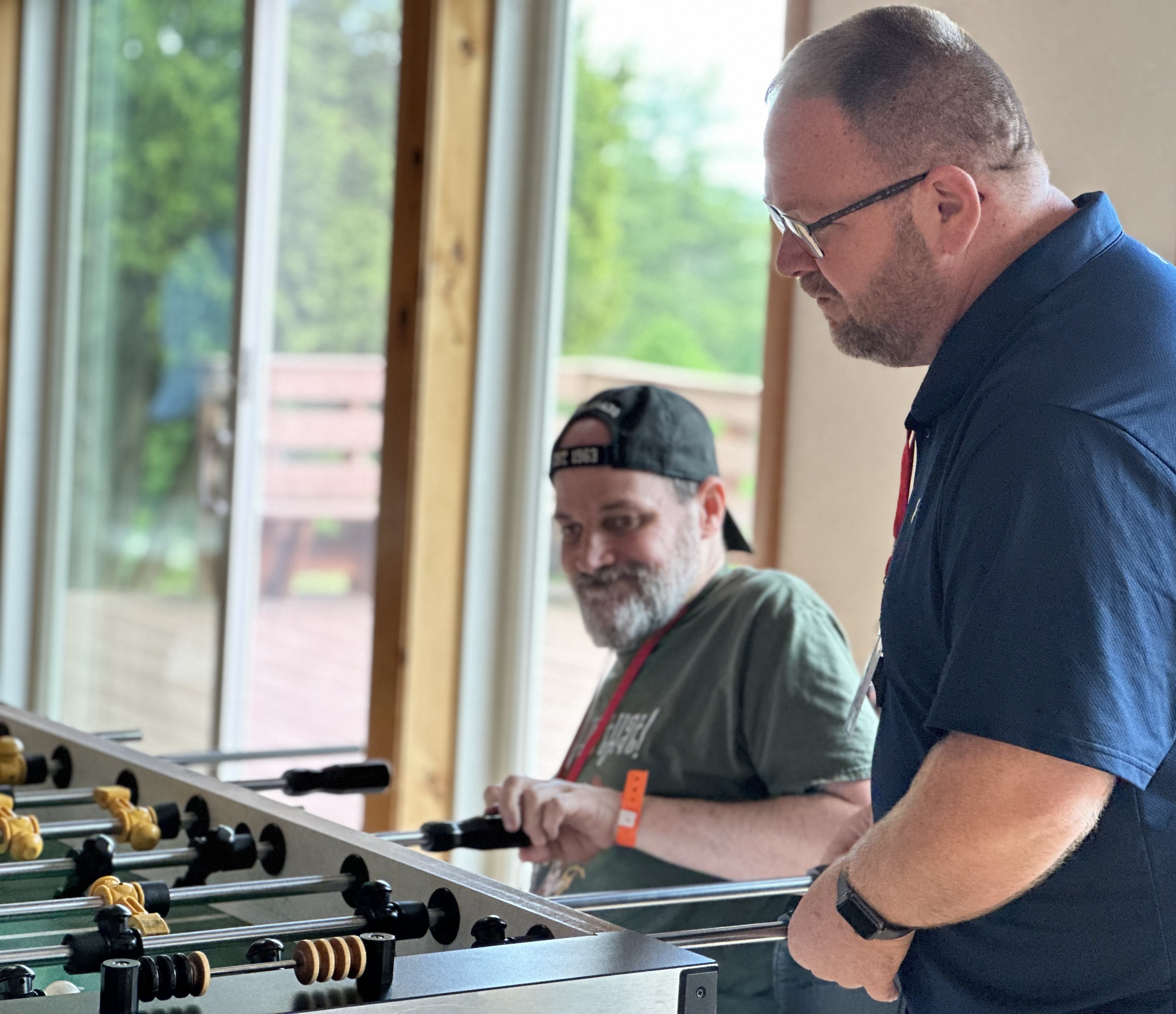 Two men, one standing, one sitting, playing fooseball