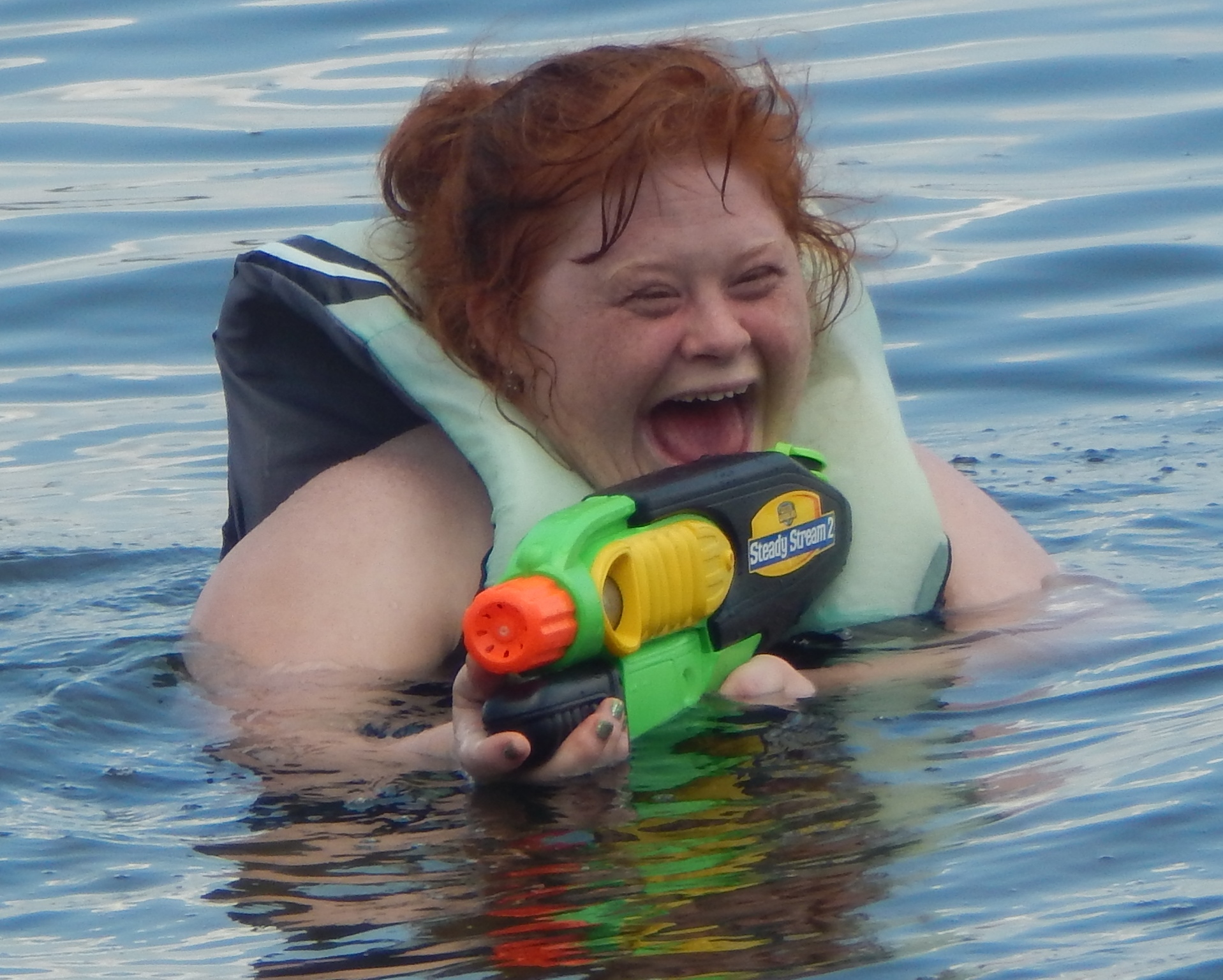 Girl holding squirt gun standing in a lake laughing