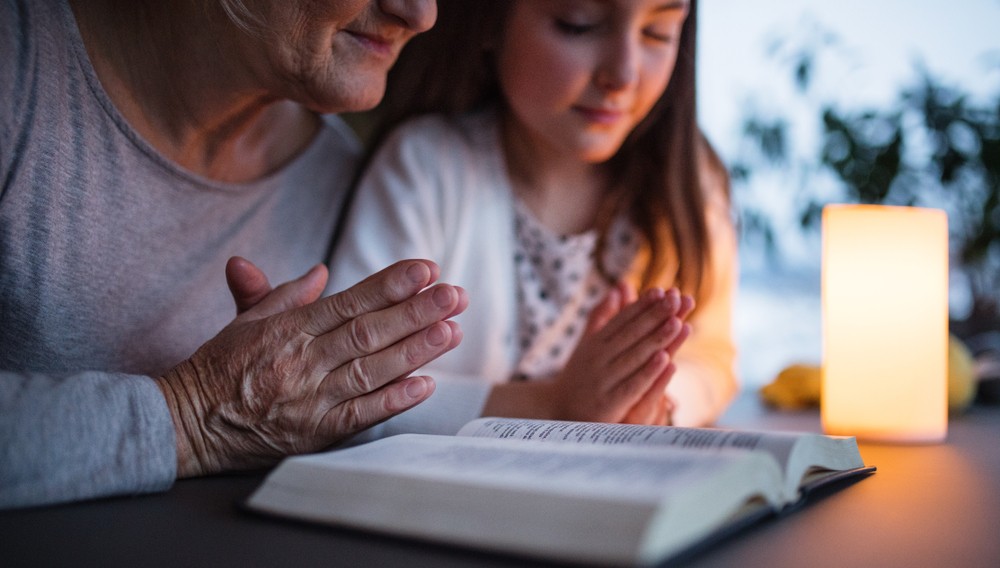 Old woman and young girl praying and reading bible