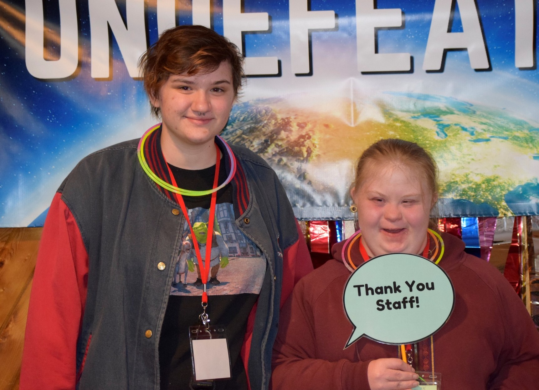 One woman and one girl with a disability, holding a sign that says thank you staff