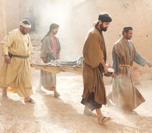 4 men carrying a main on a flat board who looks unable to walk