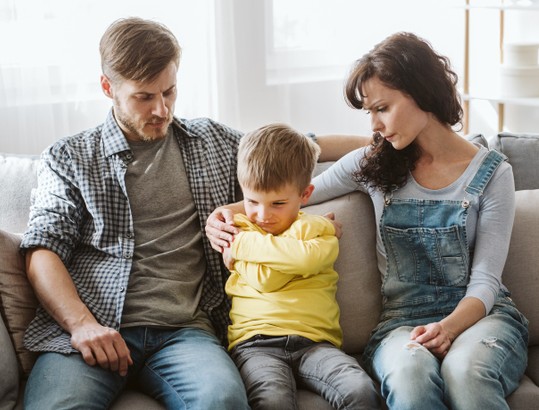 Man and woman sitting behind a boy with his arms crossed offering comfort