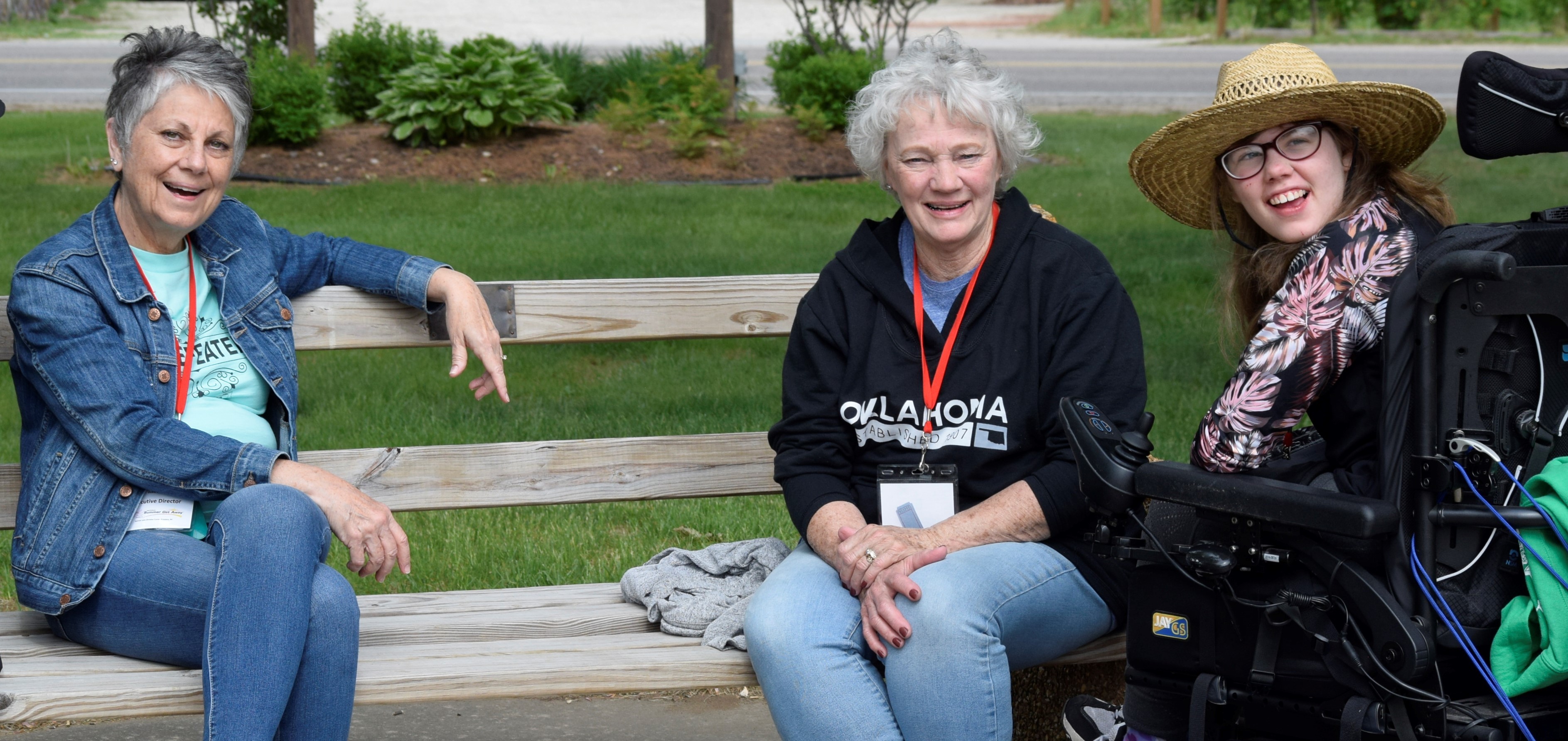 Two women sitting on a bench on girl sitting in a wheelchair all smiling for the camera