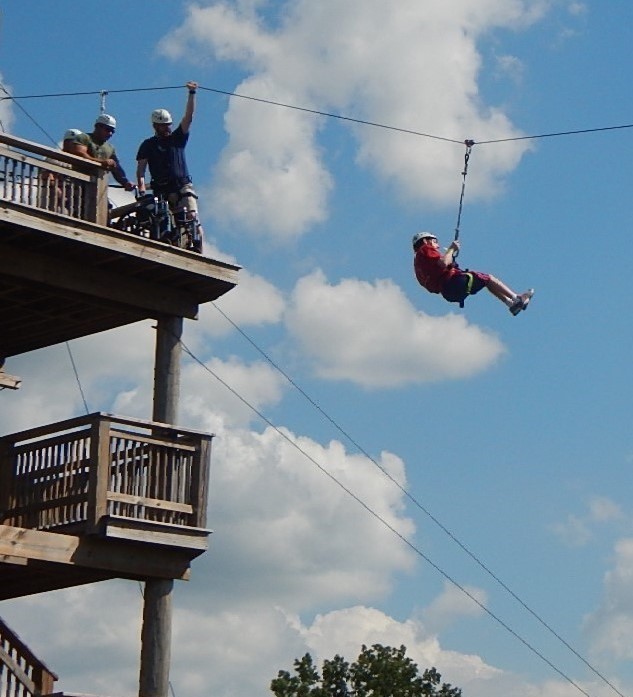 A person going down a zip line while the wheelchair they used is still on top platform