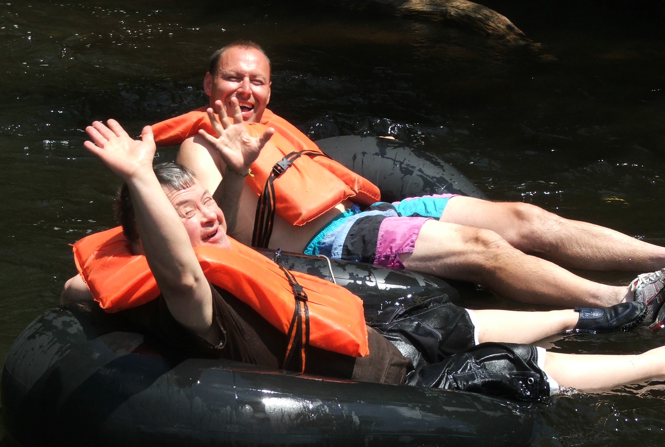 Two guys one who has a disability waving while sitting inside inner tubes floating down a rive