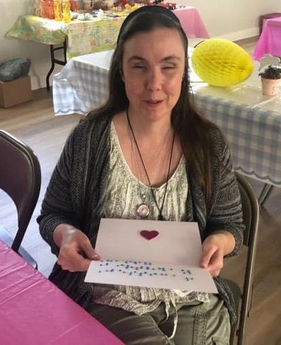 Woman who is blind smiling holding up a hand-made card easily made in braille.