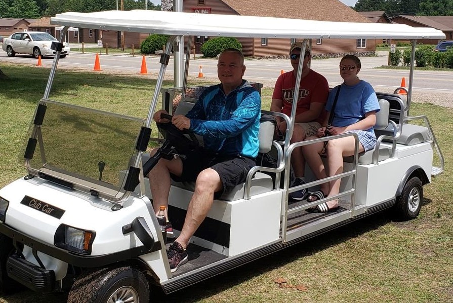 Tom Maher driving two people in the large golf cart