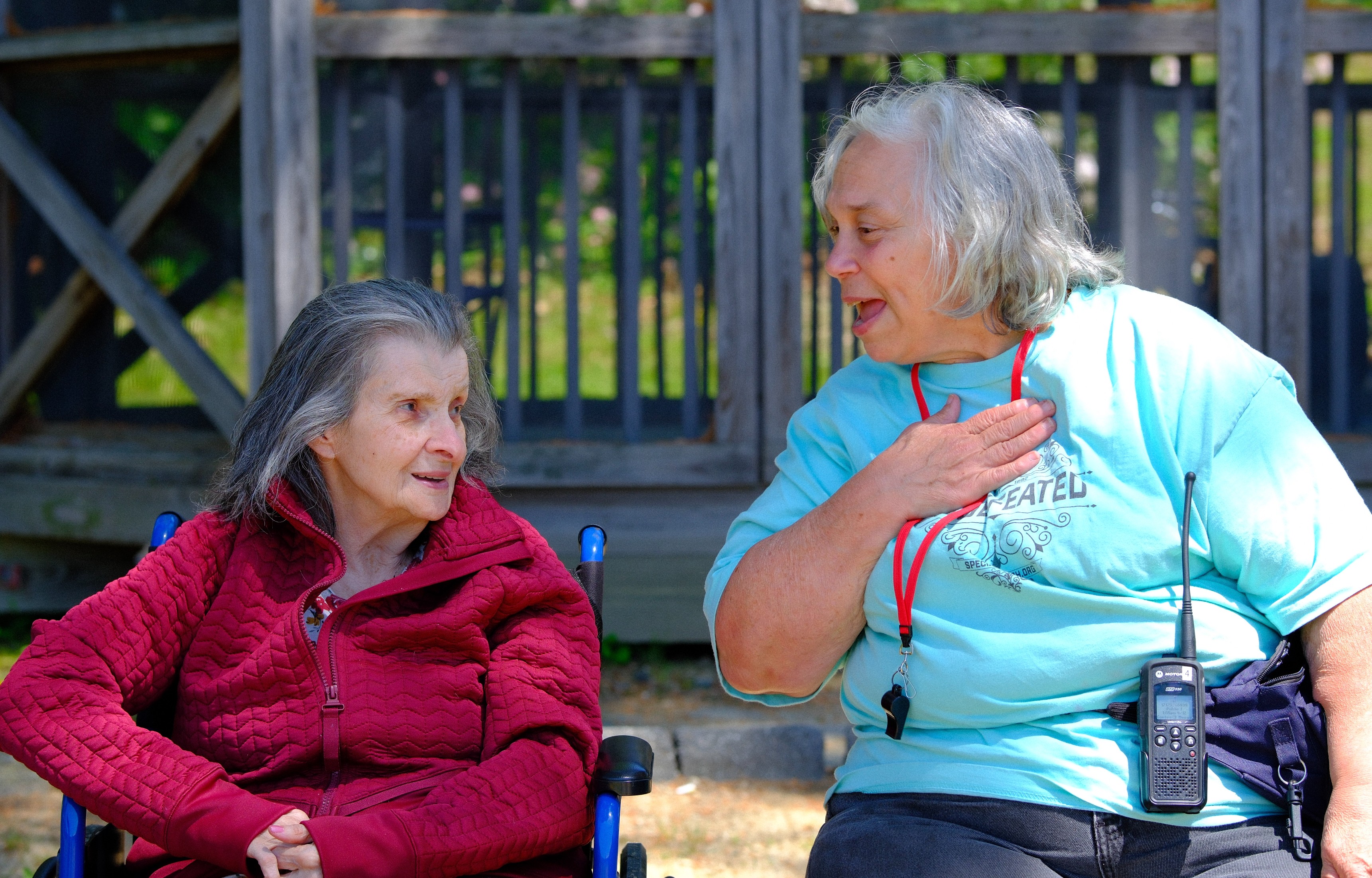 One woman sitting and talking with another woman one of which is in a wheelchair