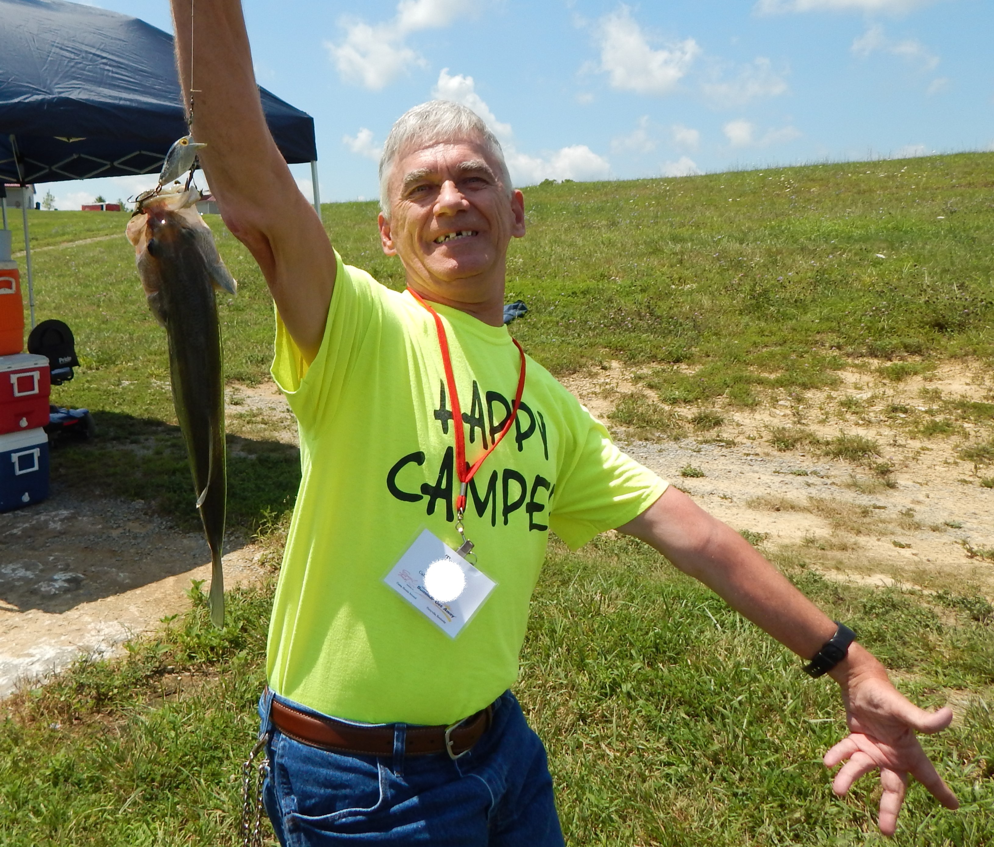 Man with a large fish a smile and a shirt that reads happy camper